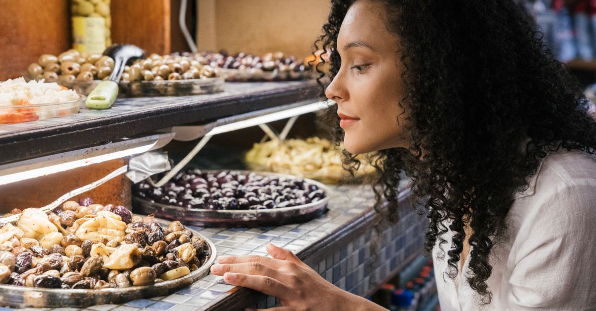 A woman observes a display filled with a variety of olives and other foods.